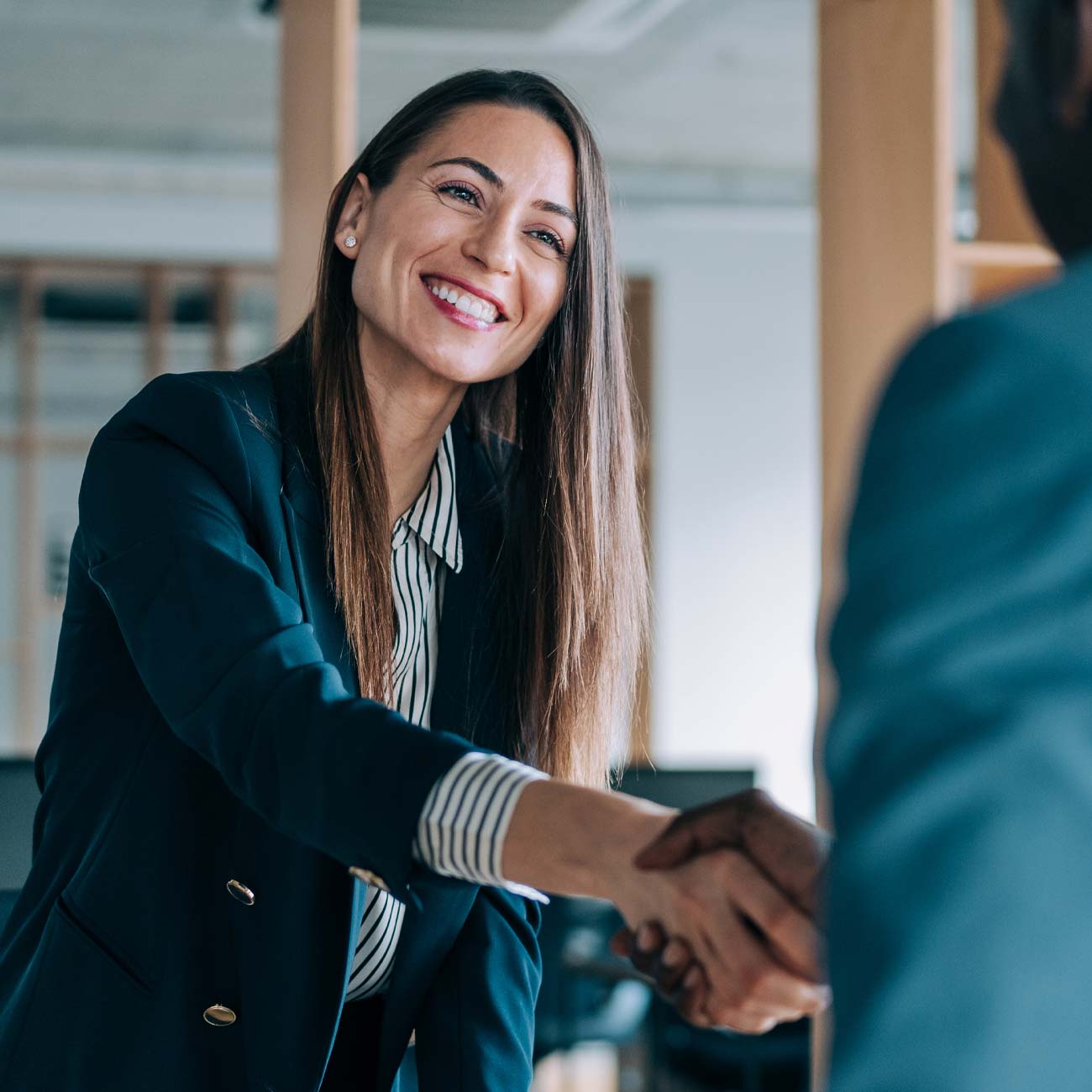 Brunette business woman in a suit, smiling, shaking hands