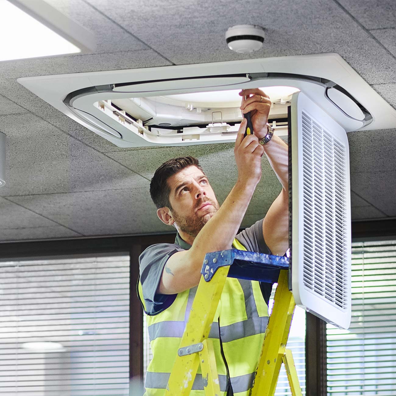 A construction worker on a ladder works on a light fixture