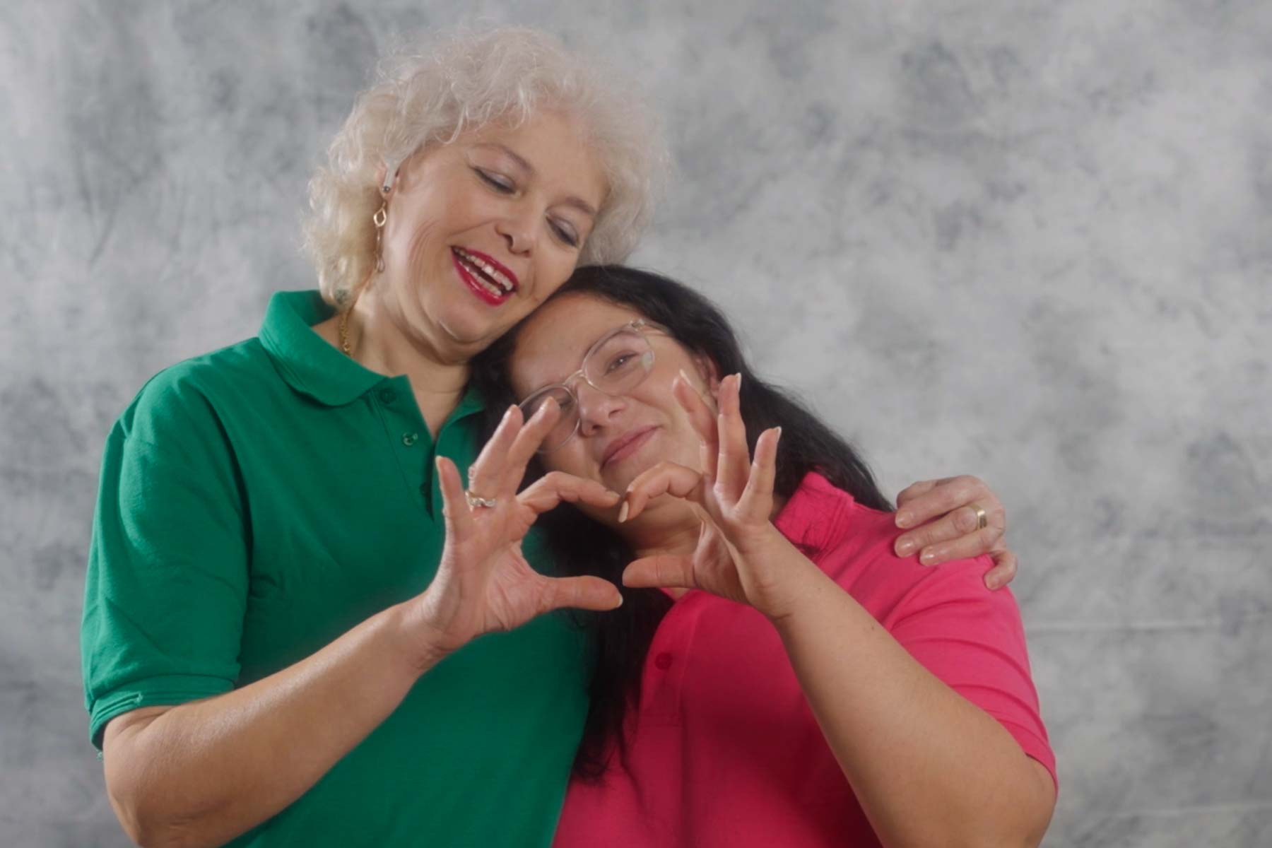 Two women hug and make a heart shape with their hands