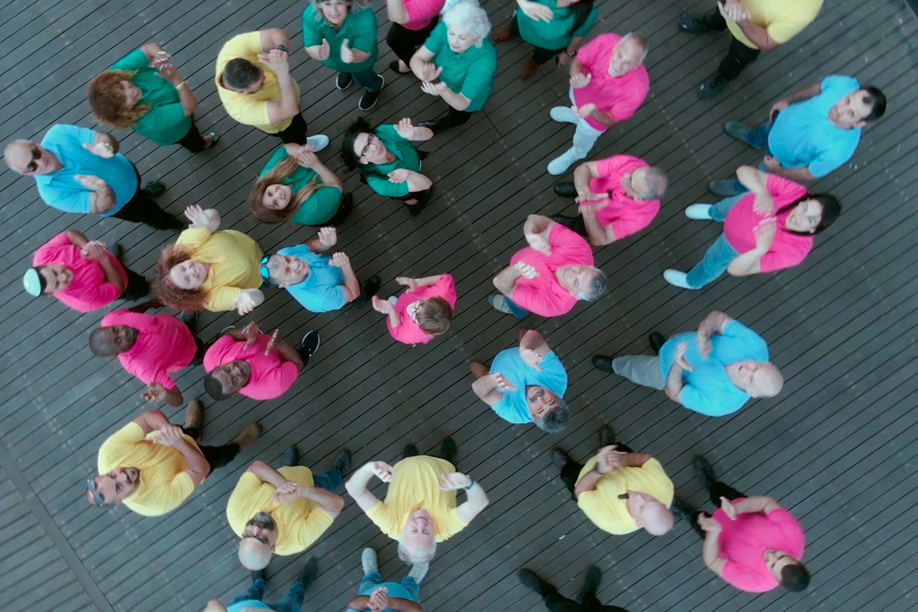 A group of Electra FM employees stand together wearing colorful polo shirts